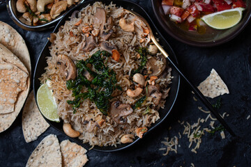 Indian rice and mushroom pilaf along with salad and popadum crackers on dark backround, copy space