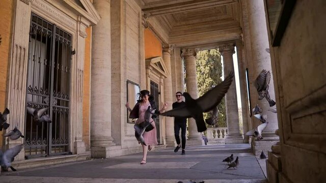 Cheerful man and woman run towards a flock pigeons to scare them cross a bridge. Romantic couple running among pigeons holding hands. guy and the girl the birds. Rome, Italy. Slow motion