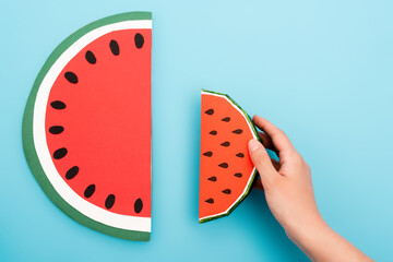 partial view of female hand with paper watermelon slices on blue background