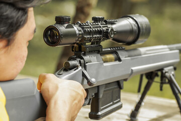 Military sniper with his precising sniper rifle aiming through scope and shooting in the shooting range 