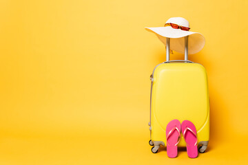 yellow travel bag with flip flops, sun hat and sunglasses isolated on yellow