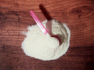 A heap of organic milk formula for infants, with measuring spoon, on brown wood background