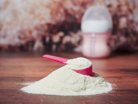 A heap of organic milk formula for infants, with measuring spoon, on brown wood background
