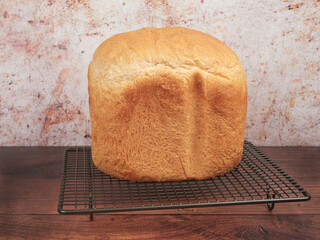 Fresh bread made at home with the bread machine, set on a gray cooling rack, on brown background - Powered by Adobe