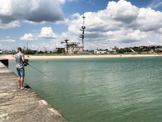 The guy is fishing on a spinning rod on the pier