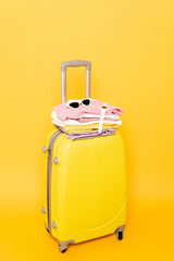 travel bag with summer clothes and accessories isolated on yellow