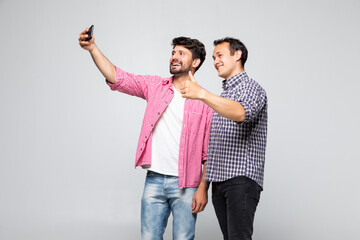 Portrait of a two excited young men taking a selfie while standing together isolated over white background