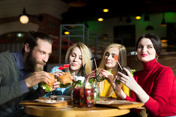 People have dinner together at a table in a cafe. Happy friends eat burgers and drink cocktails in the restaurant