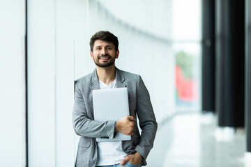 Portrait of handsome businessman standing smiling while using laptop in office