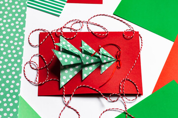 Fototapeta premium Handmade New Year postcard with paper christmas fir tree. Holiday idea for family time and gift for beloved. Fine motor skills, creativity development and fun. Traditional colors: green, red.