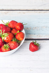 Berries of ripe strawberries lie in a white high plate, which stands on a light wooden background. Place for copy space