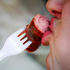 The girl bites off a grilled sausage on a fork. Girl eating a sausage close up