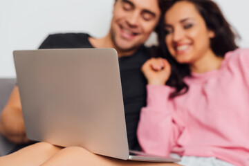 Selective focus of positive couple using laptop on sofa isolated on grey