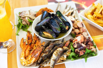 A sea food plate with grilled, fried and marinated fish, shrimps, squids and cooked mussels with wine and garlic
