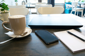 cup of coffee, latte, laptop, phone and notebook for remote distance work job on wooden table in cafe