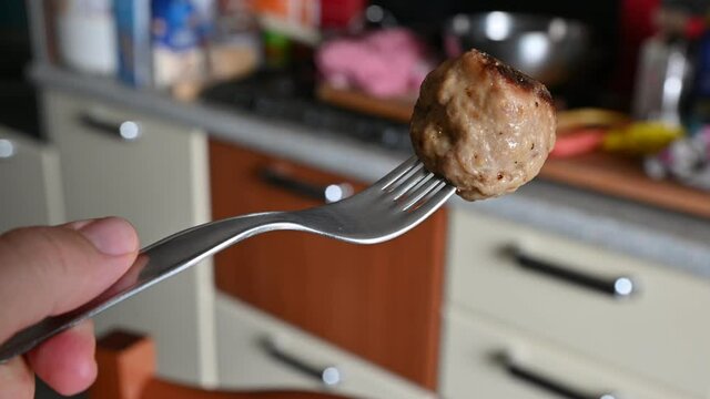 In the blurred background of a kitchen a close-up image of a meatball skewered by a fork appears.
