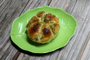 Korean garlic cheese bread is made from bread, cream cheese, garlic, parsley, and honey served on a leaf-shaped green plate on a wooden table.