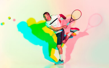 In jump. One caucasian man playing tennis on studio background in colorful neon light. Fit young professional male player in motion or action in sport game. Concept of movement, sport, healthy