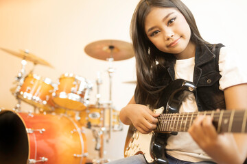 Fototapeta na wymiar A portrait of a cute Asian girl with long hair playing an electric guitar in a music practice room.