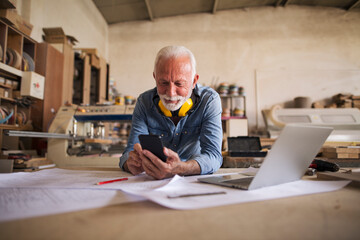 Likeable older carpenter is looking at the cellphone and smiling