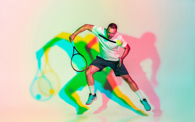 Fototapeta na wymiar In jump. One caucasian man playing tennis on studio background in colorful neon light. Fit young professional male player in motion or action in sport game. Concept of movement, sport, healthy