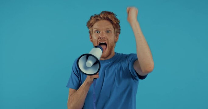 bearded redhead man yelling in megaphone isolated on blue