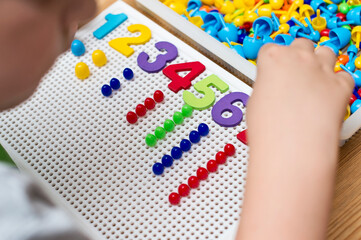 By provided numbers boy inserting pins. counting game. mathematical task. play at home. way of learning.