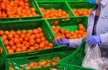 Senior woman stay safe wearing medical mask to prevent Covid-19  and rubber gloves choosing vegetables in a supermarket -safe and healthy pensioner concept