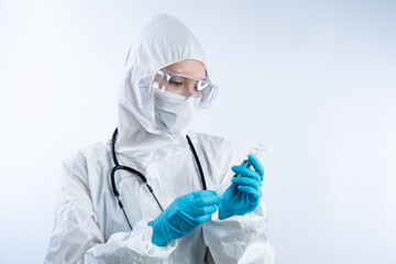 Female doctor in PPE (personal protective equipment), gloves face mask and safety glasses holding coronavirus vaccine bottle and needle.