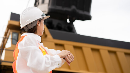 Worker looking at watch on wrist in lignite or coal mining with the truck transporting coal.