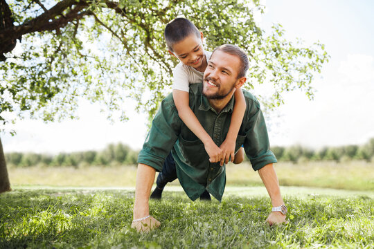 Young Man Doing Push-ups In The Street With A Child On His Back, Father And Son Go In For Sports