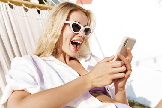 Image of charming excited woman using cellphone while lying in hammock