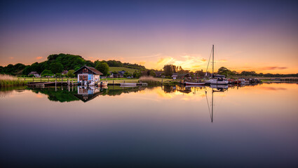 Panoramic shot of a sunset with a cabin and a boat with their reflections on the sea.