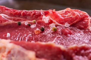 Fresh Beef for Ribeye Steak Sprinkled with Spices: Large Crystals of Himalayan Pink Salt, Smoked brown Salt Crystals, Green, White, Black, Pink Peppercorns. Selective Focuse. CloseUp.