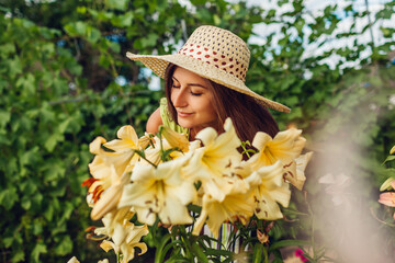 Young woman smelling flowers in garden. Gardener taking care of lilies. Girl growing plants. Gardening concept