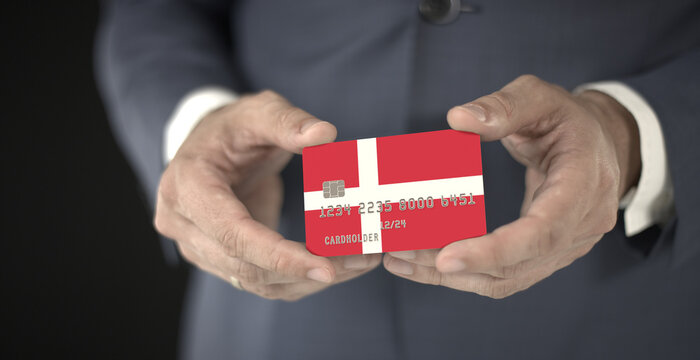 Businessman holding credit card with printed flag of Denmark, fictional numbers
