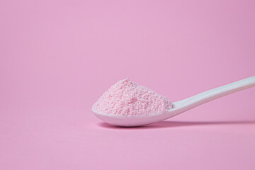 A spoon with pink powder on a pink background. Gelatinous dessert mix of pink color, with cherry...