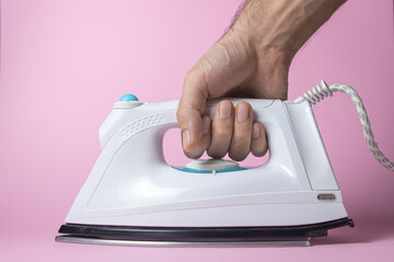 White iron on a pink background. The hand holds the iron by the handle. Old style iron, retro style.