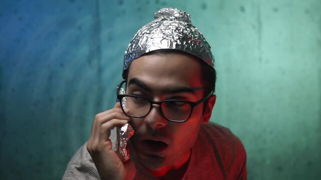 Insane young man wearing a tin foil cap and covering hisphone with aluminium foil because he is afraid of the waves and the government spying on him.