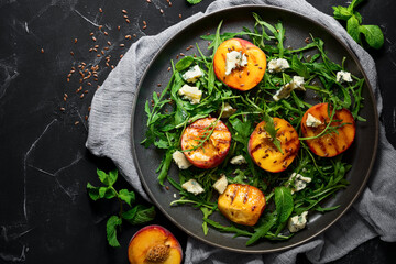 Grilled peach, arugula and blue cheese salad on a black stone background. Fresh diet dish. Top view, flat lay, copy space.