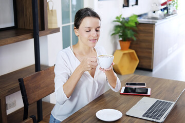 Smiling Caucasian woman happy with smell the aroma of hot coffee in the morning at cafe. She is relaxing with social online on laptop, tablet and smartphone on holiday. Lifestly and technology concept