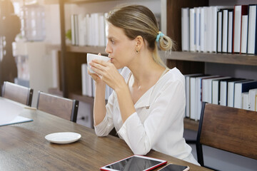 Smiling Caucasian woman happy with smell the aroma of hot coffee in modern cafe. She is relaxing with social online on tablet and smartphone on holiday. Lifestly and technology concept