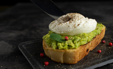 Knife blade cuts poached egg on avocado toast