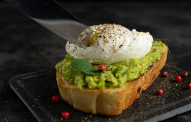 Knife blade cuts poached egg on avocado toast