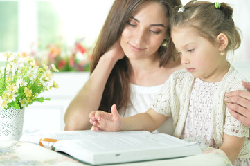 Portrait of little cute girl with mother reading book at home