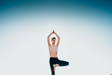 Young man in a Namaste greeting position while freeing his mind from worries in tree pose.