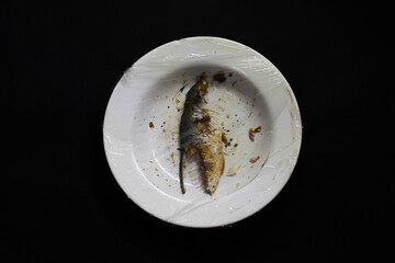Top view of Incomplete fried makerel in a plate with plastic wrapped