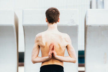 Yoga posture inverted prayer or Namaste hands on the back performed by a young man outdoors.