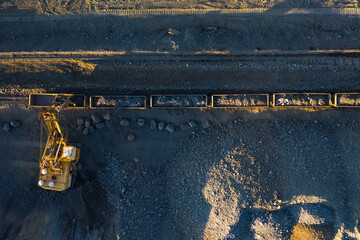 Excavator loads ore into freight cars aerial top view.