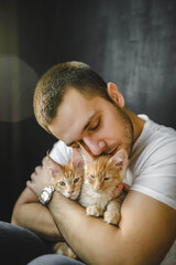Handsome young man with a beard hugging red-headed maine coon cat. guy in white T-shirt holding two kittens in hands man hugs cats tightly tenderly